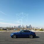 Modern blue car parked in front of a city skyline with a glowing digital shield symbol in the sky, representing vehicle protection and coverage from the best car insurance companies.