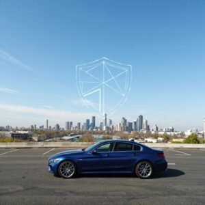 Modern blue car parked in front of a city skyline with a glowing digital shield symbol in the sky, representing vehicle protection and coverage from the best car insurance companies.